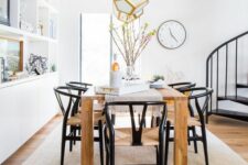 a chic modern dining space with a large storage unit, a light-stained table and black wishbone chairs, faceted pendant lamps