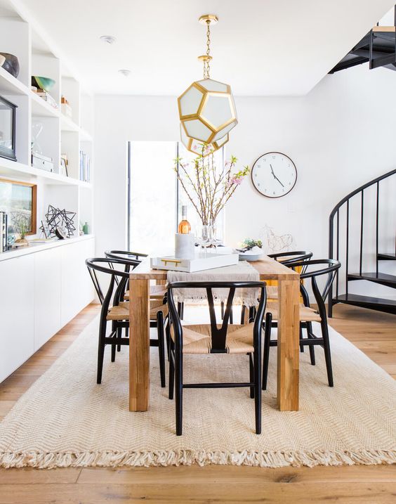 a chic modern dining space with a large storage unit, a light-stained table and black wishbone chairs, faceted pendant lamps