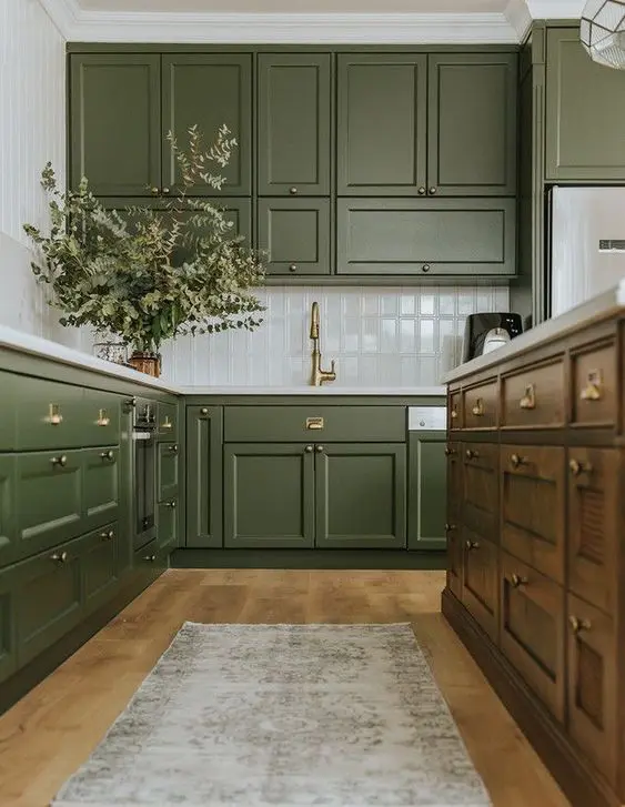 A chic olive green farmhouse kitchen with shaker cabinets, a white tile backsplash, a dark stained kitchen island and a printed rug
