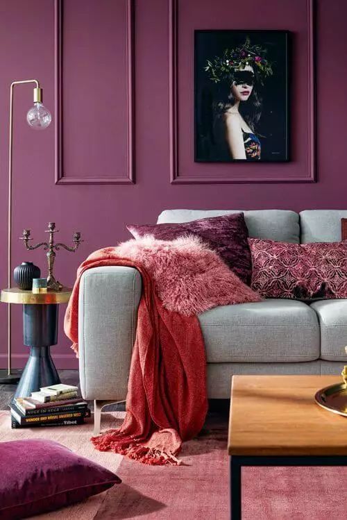 a colorful living room with purple molded walls, a grey sofa, a coffee table, an elegant side table and bold textiles