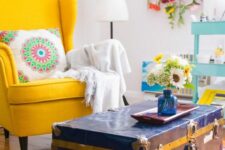 a colorful space with a yellow Strandmon, a navy chest as a coffee table, a printed rug, a floral decoration on the wall