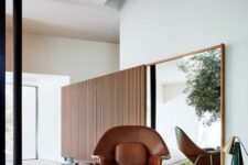a contemporary space with a mirror in a frame, a brown leather Wumb chair and ottoman, a round coffee table and a table lamp