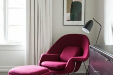 a contrasting nook with a burgundy Wumb chair and ottoman, a black floor lamp and a contrasting artwork, a black dresser