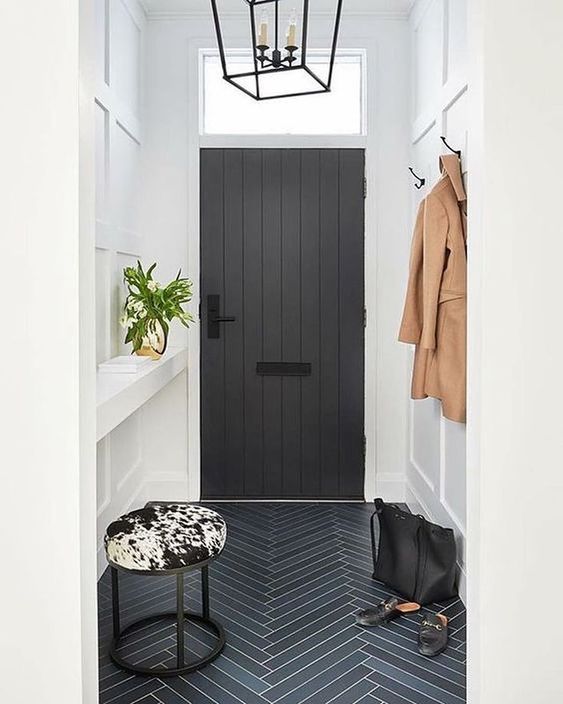 a cool black and white entryway with a black door and black and grey tiles, a built-in console, a printed stool and a rack