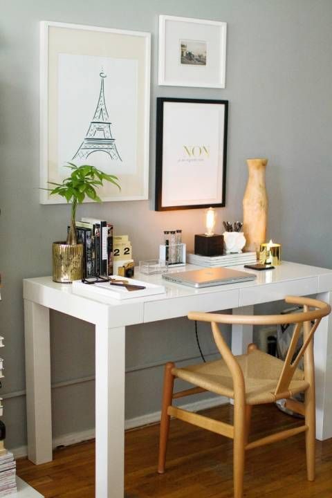 a cool working space with a sleek white desk, a wishbone chair, a mini gallery wall, candles and vases is very glam