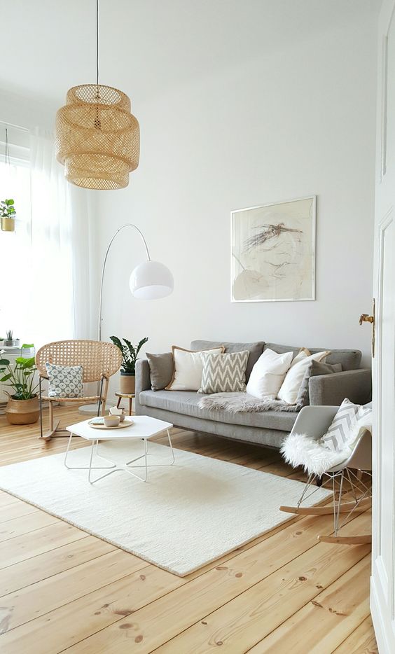 A cozy light filled living room with a grey sofa, a rattan and a rocker chair, a hexagon coffee table and a woven pendant lamp