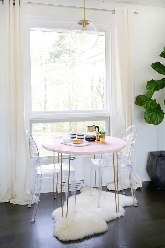 a cozy little breakfast nook with a pink hairpin leg table, ghost chairs, a clear pendant lamp and a faux fur rug