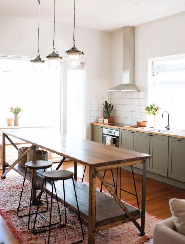 A cozy mid century modern kitchen with lower olive green cabinets, a vintage wooden kitchen island, wooden stools and vintage pendant lamps