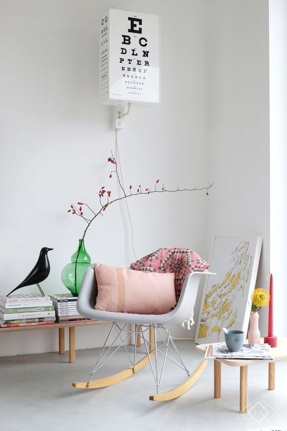 a cozy nook with a grey Eames rocker, a side table, a bench with magazines and bright candles and pillows is cool