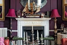 a deep purple living room with an ornated fireplace, red sofas, a printed ottoman, vintage lamps and a mirror