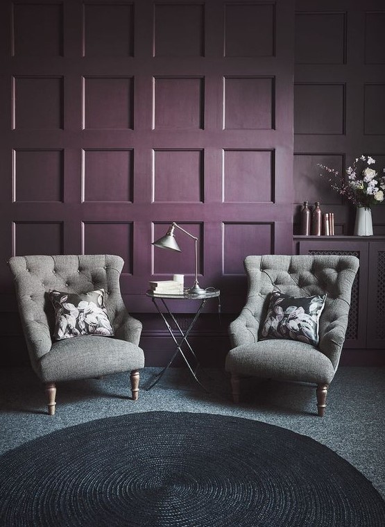 a deep purple paneled accent wall, grey wingback chairs, a side table with a lamp and a black woven rug for a refined space