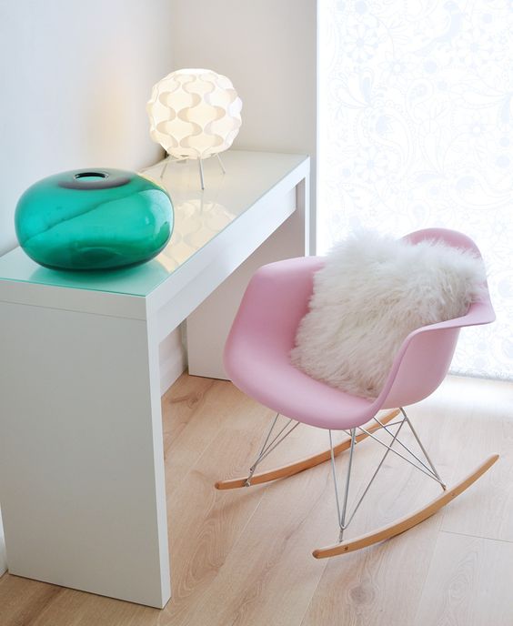 a delicate space with a white IKEA desk, a pink Eames rocking chair, a retro table lamp and a green jar