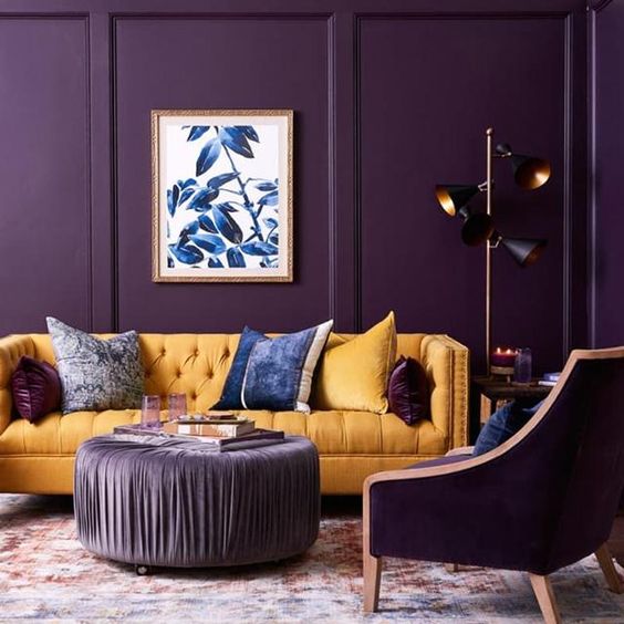a dramatic purple living room with a matching chair, a yellow sofa, lilac ottoman, blue touches and a black floor lamp