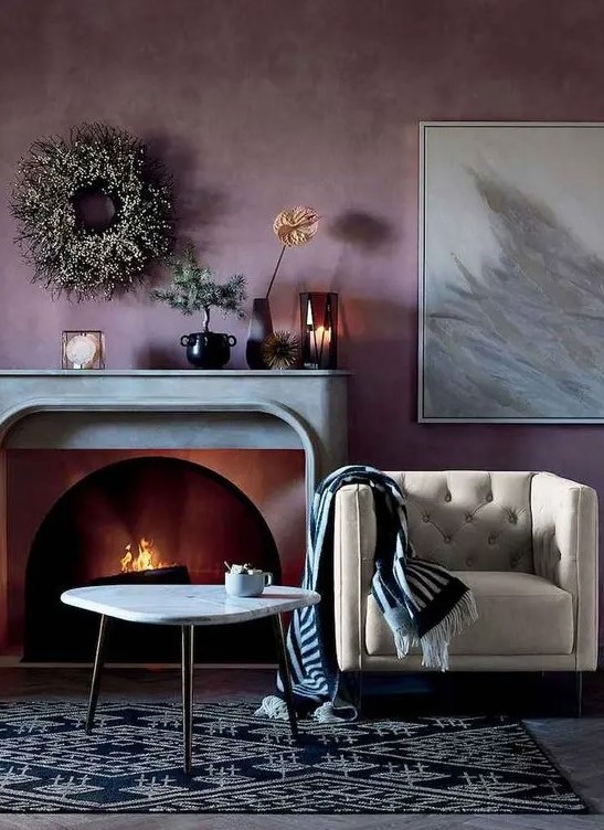 a dreamy living room with a pale purple accent wall, a fireplace with a stone mantel, a creamy chair, a printed rug and some lovely decor