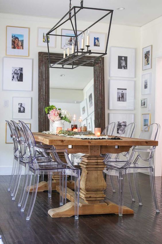 a farmhouse dining room with a stained rustic dining table, ghost chairs, a chic chandelier and photos all over the walls