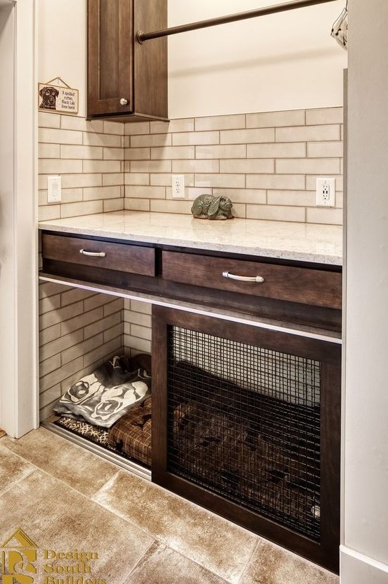 A farmhouse mudroom with dark stained cabinets, neutral tiles, a built in dog crate with blankets plus a sliding door