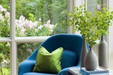 a glazed space with a blue Wumb chair and ottoman, side tables and greenery and books is amazing for reading here