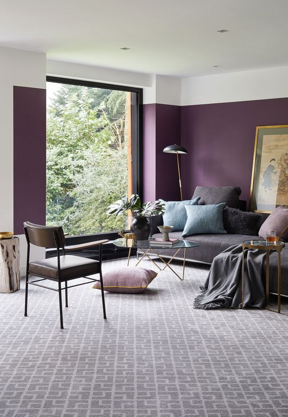 a gorgeous living room with purple color block walls, a grey sofa with pillows, a glass coffee table, a leather chair and a printed rug
