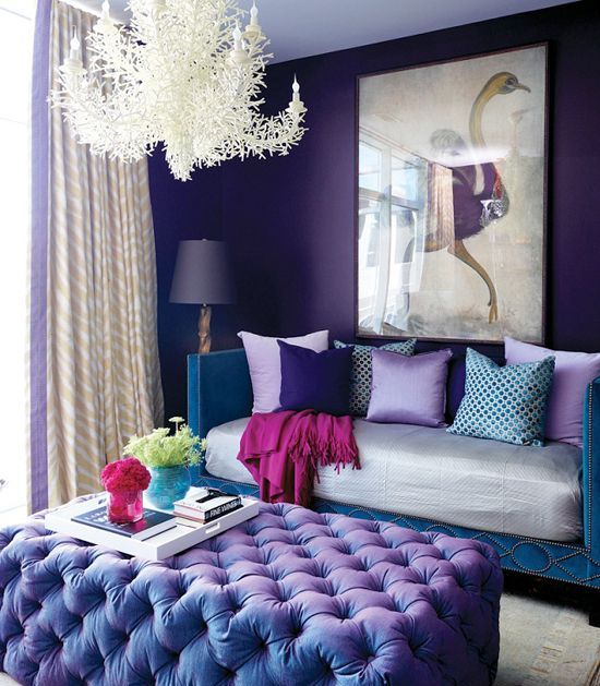 a jaw-dropping living room with violet walls, a teal sofa with lilac and blue pillows, a purple ottoman, a unique coral chandelier