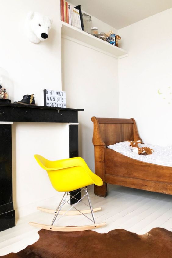 a kid's room with a faux fireplace, a stained bed, a yellow Eames rocker, a couple of shelves and toys