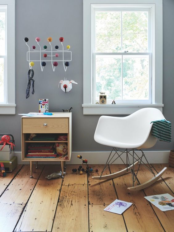 a kids' space with a stained cabinet, a white rocking chair, some toys, a rack and kids' drawings