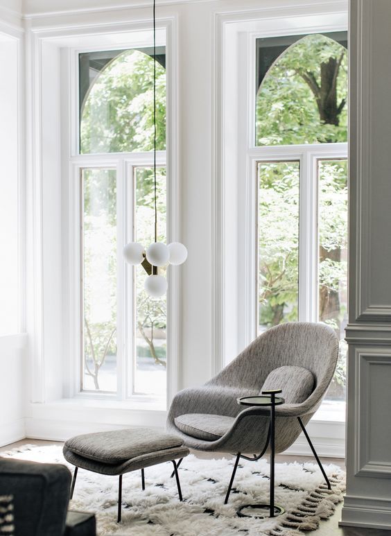 A light filled nook with a fluffy rug, a grey Wo,b chair with an ottoman and a low pendant light to read books