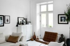 a light-filled Scandinavian living room with a neutral sofa, a couple of coffee tables, a white Eames rocking chair, a leather one and some artwork