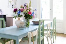 a light-filled dining space with a blush sideboard, a blue dining table and mismatching green and white chairs, a pendant lamp with a blue glass lampshade