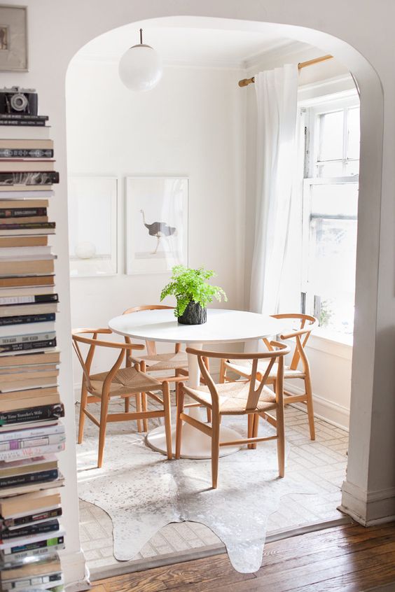 a light-filled dining space with a round table, light-stained wishbone chairs, a rug and a mini gallery wall