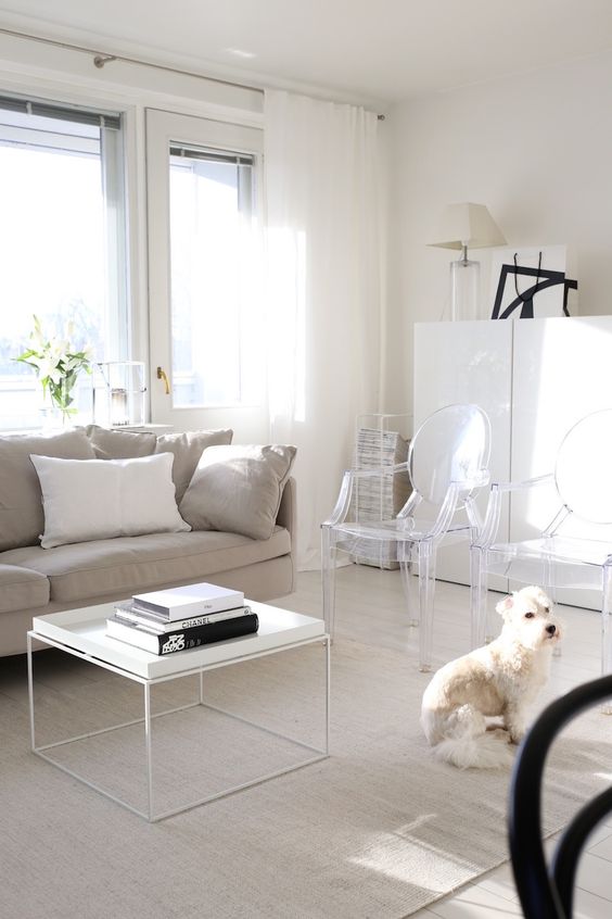 A light filled living room with a greige sofa, a white coffee table, ghost chairs, a white storage cabinet and black touches