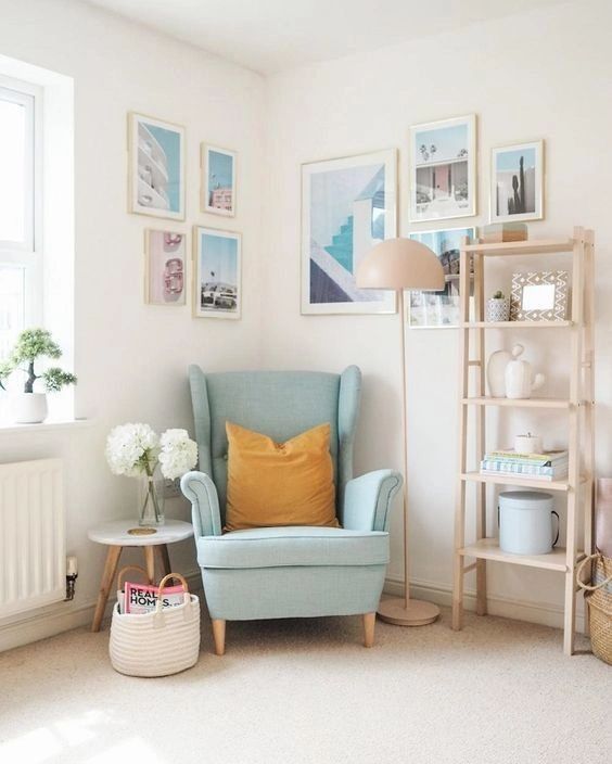 A light filled nook with a blue Strandmon chair, a side table, a light stained shelving unit, a gallery wall on two walls