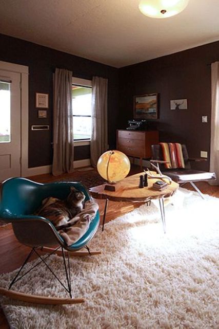 a mid-century modern living room with graphite grey walls, a mid-century modern sideboard, a grey chair, a teal Eames rocker and a coffee table