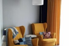 a mid-century modern living room with yellow Strandmon chairs, bright pillows and blankets, a bold printed rug and some lamps