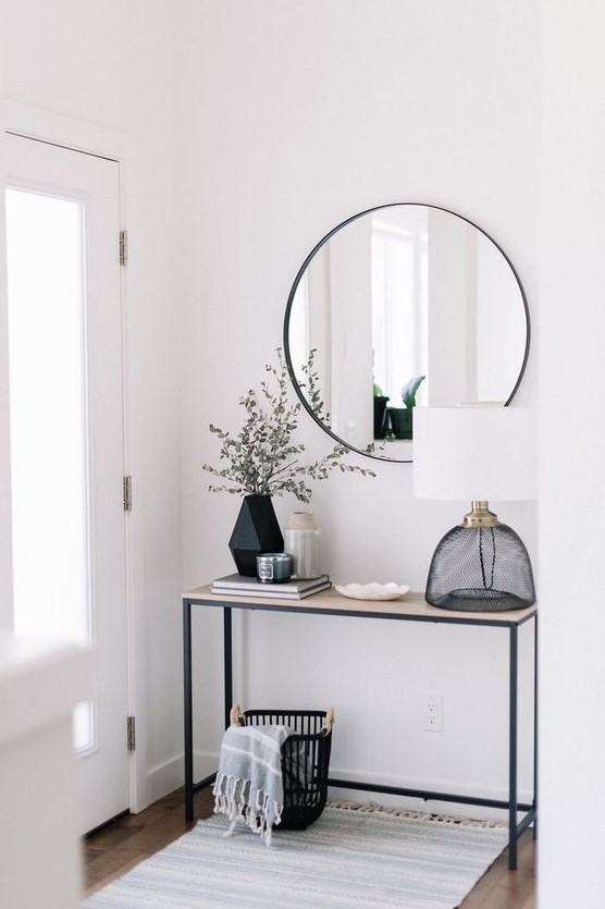 a minimal and clean black and white entryway with a sleek console table, a round mirror, a table lamp and a geo vase