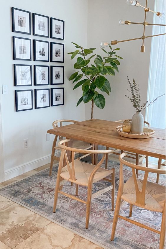 A modern Scandinavian dining space with a light stained table and wishbone chairs, a potted plant and a grid gallery wall