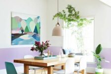 a modern dining room with color block lilac and white walls, a stained dining table, white and blue chairs, potted plants and a bold artwork