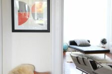 a modern space with an orange Eames rocker, leather chair and a daybed and a bold artwork that echoes with the chair