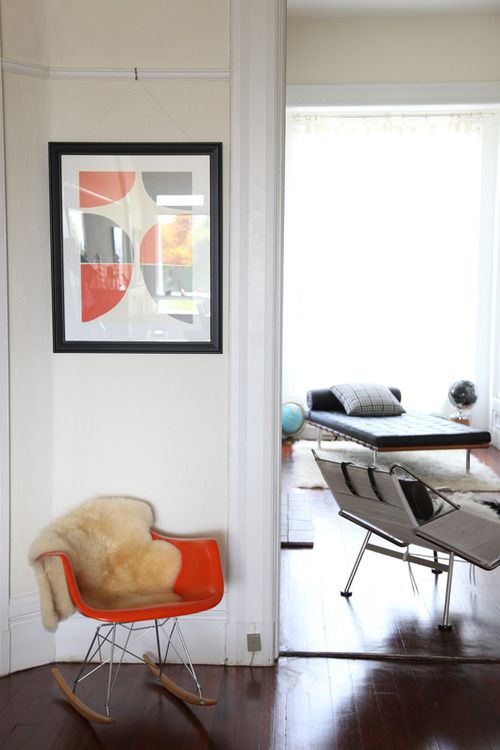 a modern space with an orange Eames rocker, leather chair and a daybed and a bold artwork that echoes with the chair