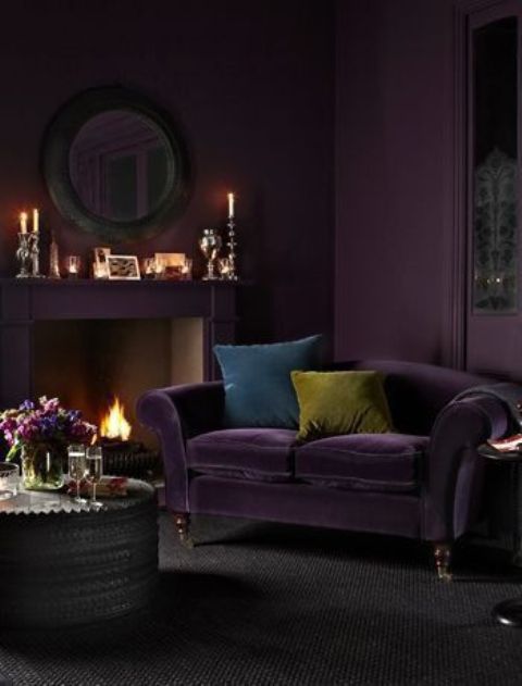 a moody deep purple living room with a fireplace, a matching sofa, a round mirror, candles and a round side table is ultimate