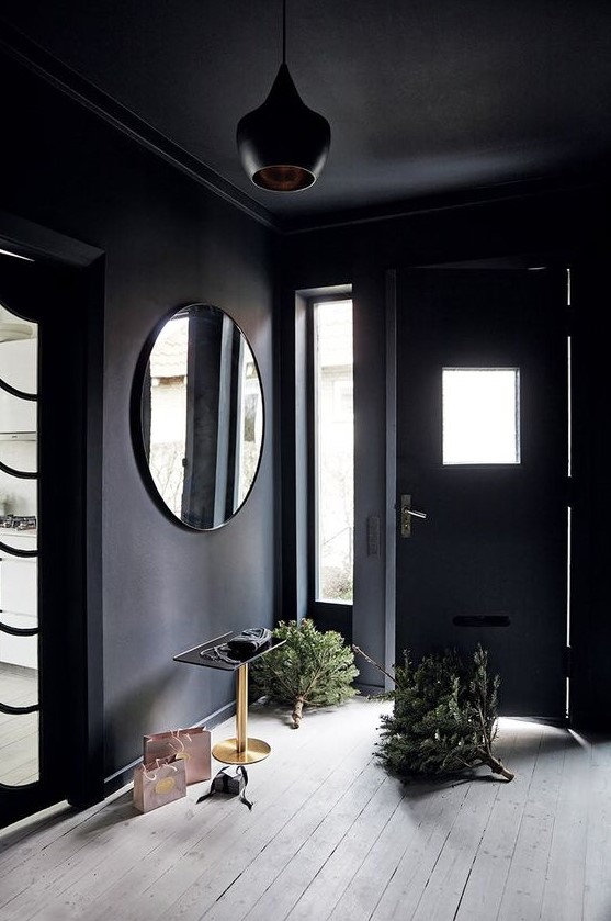 a moody entryway with black walls and a ceiling, a round mirror, a side table and a whitewashed floor is chic