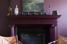 a moody living room with a deep purple accent wall, a fireplace done in the same color, leather chairs and some decor on the mantel