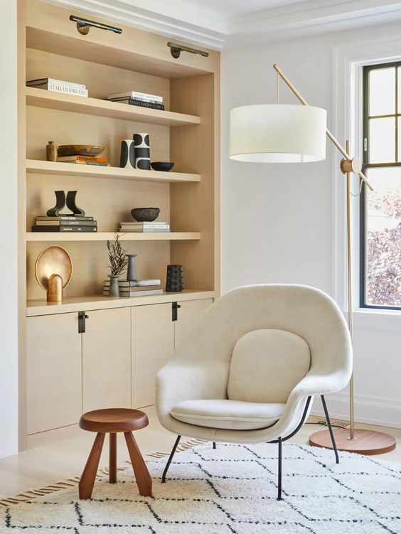 A neutral space with a light stained built in storage unit, a creamy Wumb chair, a side table and a floor lamp
