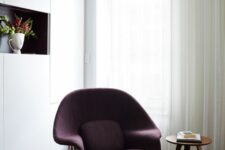 a neutral space with a sleek white storage unit, a niche shelf, a deep purple Wumb chair with an ottoman, a side table