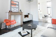 a peaceful monochromatic Scandinavian living room with orange touches – an Eames orange rocker, orange pillows and a bold artwork