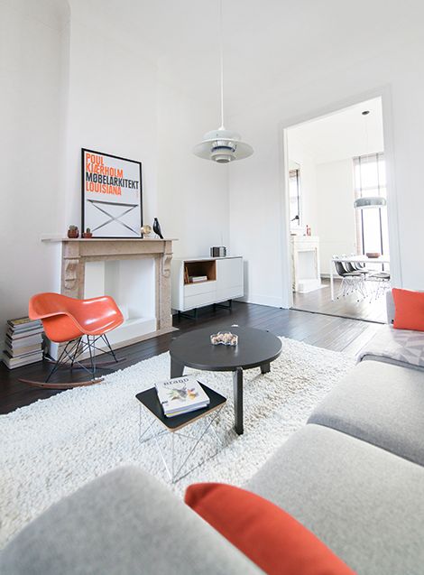 a peaceful monochromatic Scandinavian living room with orange touches - an Eames orange rocker, orange pillows and a bold artwork