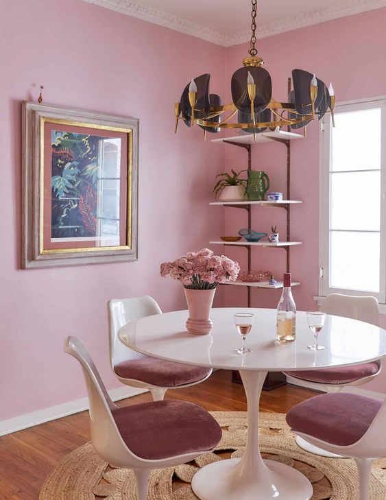 a pink dining room with open shelves, a round table, mauve chairs, a cool chandelier and a bold artwork
