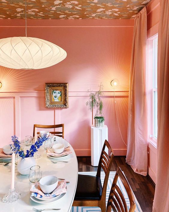 a pink dining space with a printed ceiling, paneling, an oval table, stained chairs and some pretty art