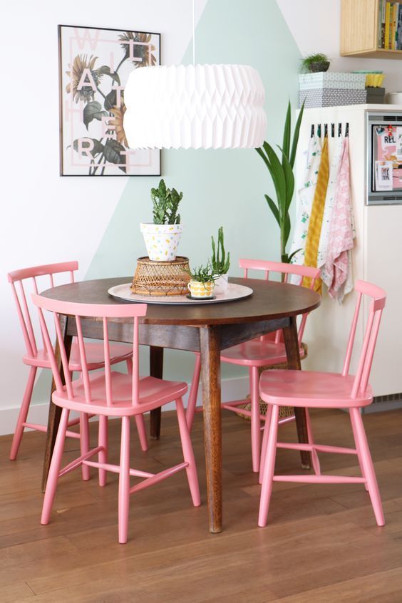 a pretty dining nook with a color block green and white wall, a stained round table, pink chairs, a pendant lamp and potted plants
