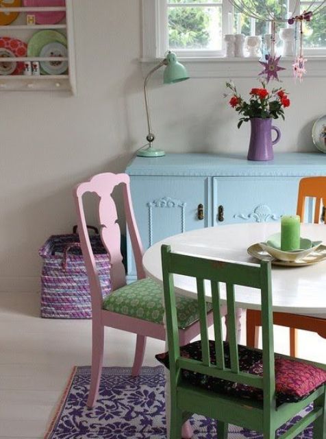 a pretty dining room with a blue credenza, an oval table, mismatching pastel chairs, a purple vase, an aqua table lamp