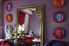 a purple living room with a floor mirror, a violet chair and a red sofa, a gallery wall of colorful plates and a gold table